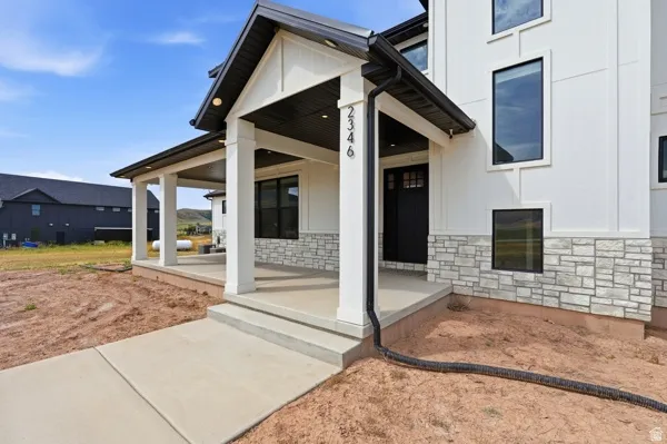Modern exterior featuring a covered front porch, white vertical siding, black-framed windows, a black entry door, and a stone facade foundation
