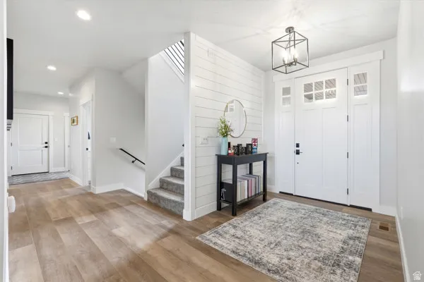 Inviting entry foyer featuring wood-finish flooring, a white paneled accent wall, and a staircase with carpeted treads and an open railing