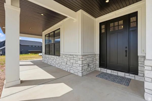 Inviting covered entryway featuring a black paneled front door with glass lites, coordinating black sidelites, and a dark wood-finish ceiling with recessed lighting