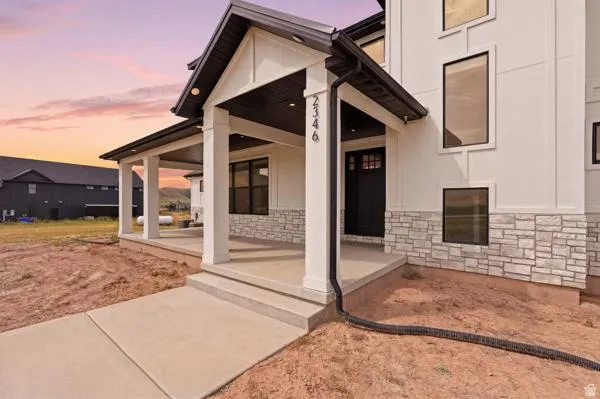 Contemporary exterior featuring white vertical siding, light-toned stone veneer accents, a dark-stained front door with transom window, black-framed windows, and an expansive covered porch