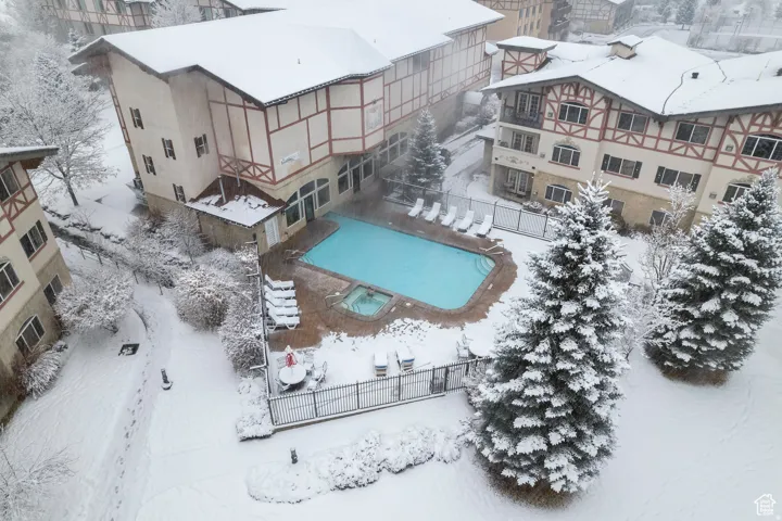 Outdoor swimming pool and spa surrounded by a paved deck and a black metal fence, all situated amidst snow-covered grounds