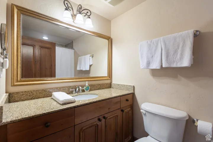 Bathroom featuring a wood-finish vanity with a speckled countertop, an undermount sink, and a framed mirror with an ornate light fixture