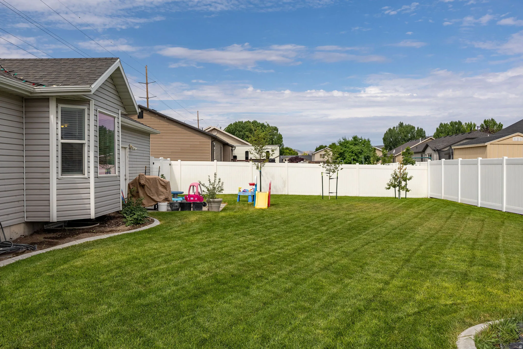 Expansive backyard featuring a manicured lawn, full vinyl privacy fencing, and mature landscaping
