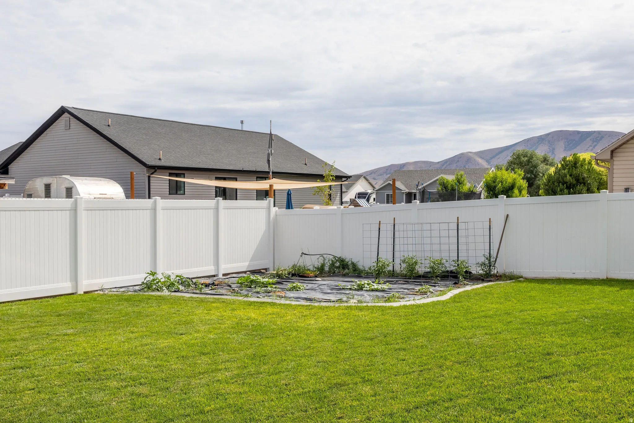 Expansive backyard featuring a green lawn, white privacy fencing, and a dedicated garden area