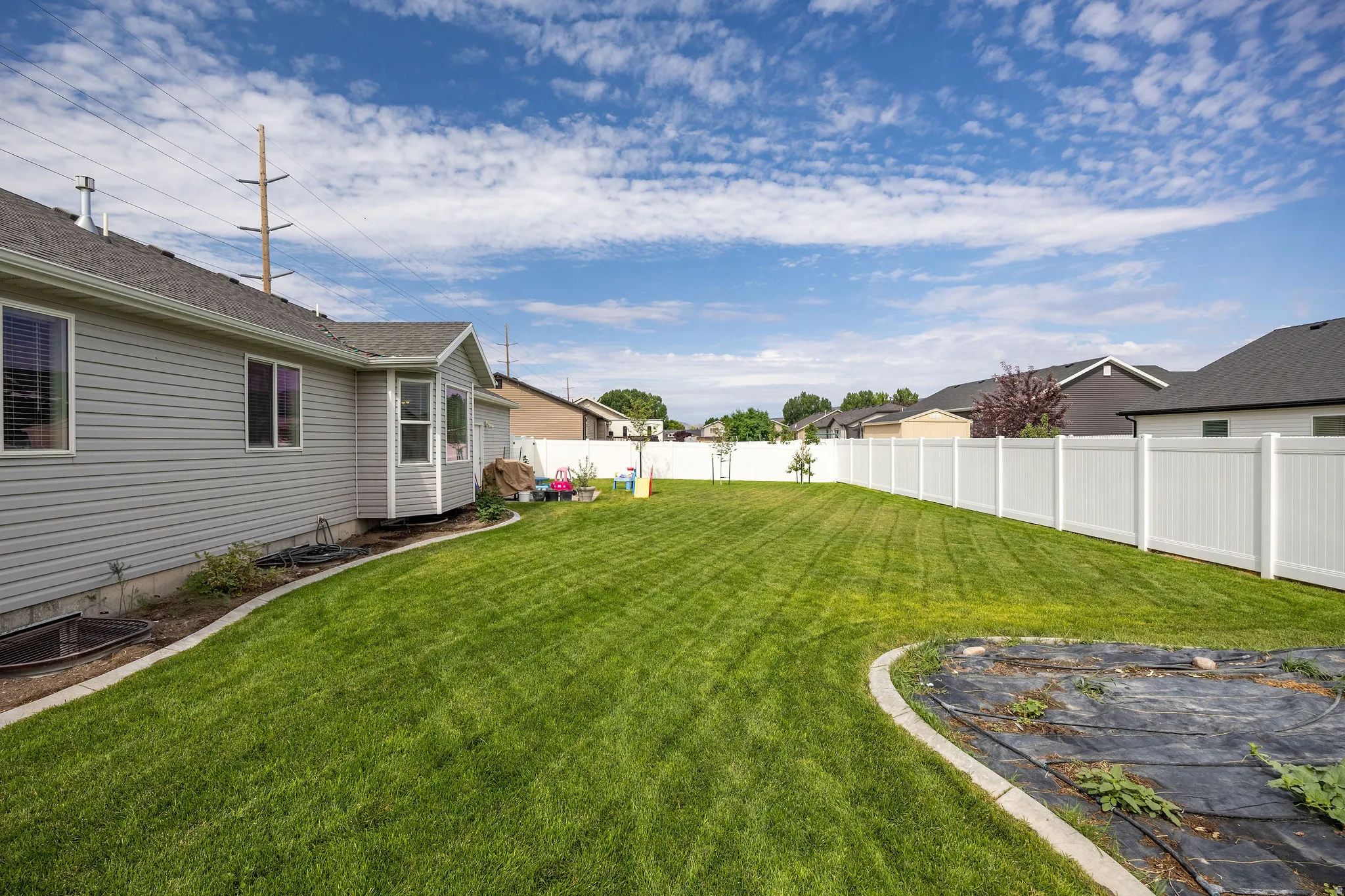 Expansive backyard featuring a manicured lawn, a full white privacy fence, and a designated planting area