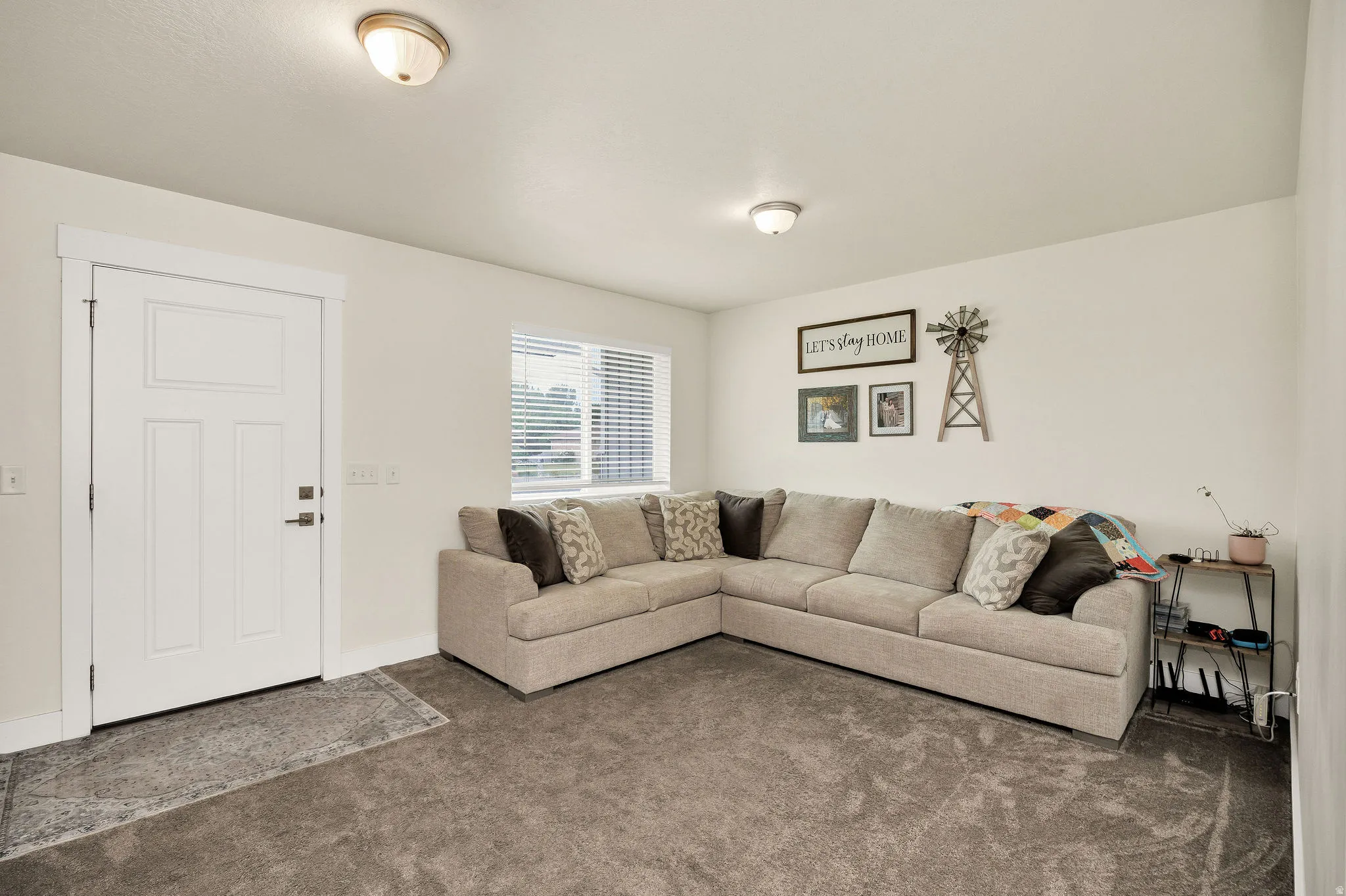 Carpeted living space with a white paneled door, flush-mount lighting, and a single window with blinds