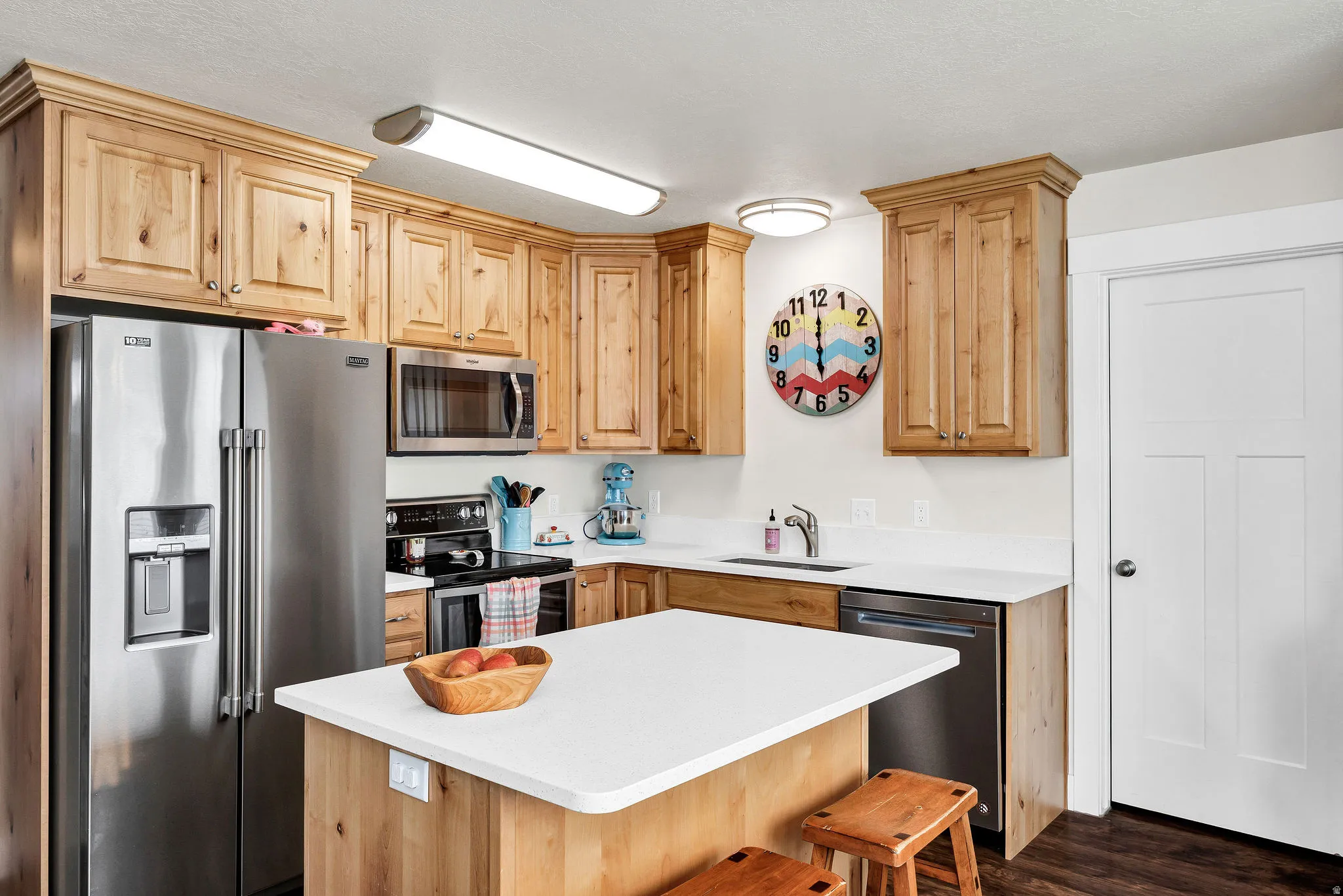 Kitchen featuring extensive wood cabinetry, stainless steel appliances, a center island with a white countertop, and wood-finish flooring