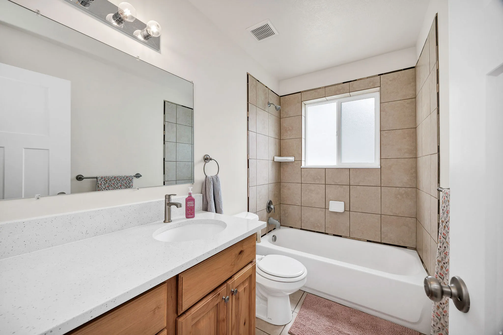 Bathroom featuring a tub/shower combination with beige square tiling, a window, and a white vanity with wood-finish cabinetry, a white countertop, and an undermount sink