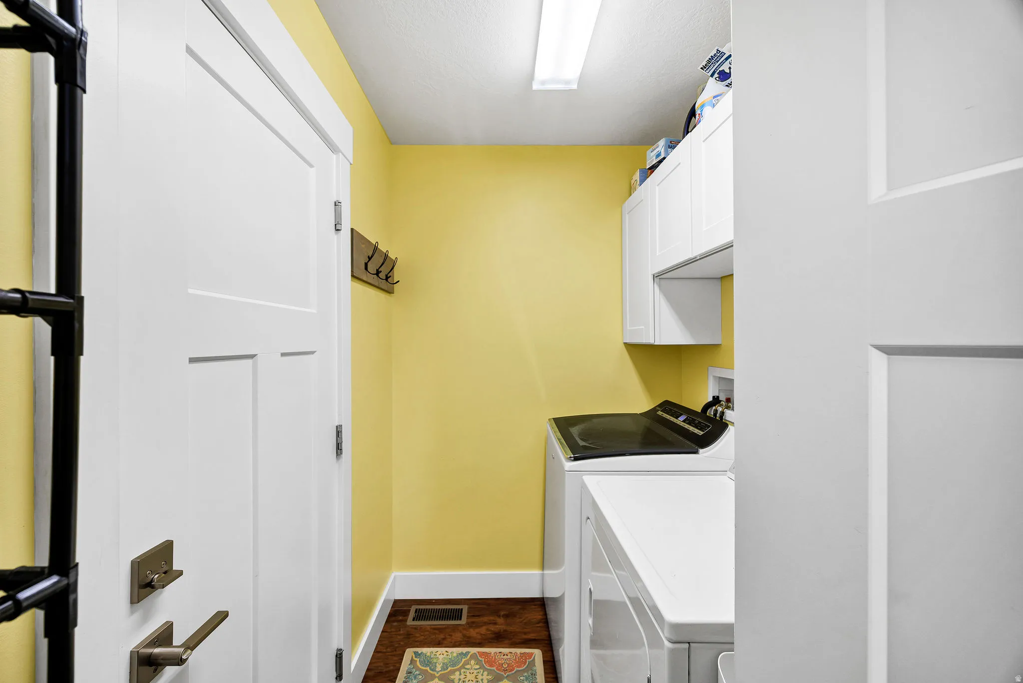 Utility space featuring overhead cabinetry, a white washer and dryer, wood-finish flooring, and bright yellow wall paint