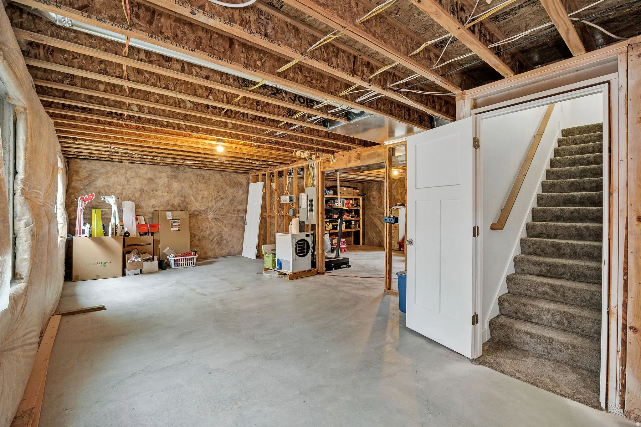 Unfinished basement featuring exposed wood joists, concrete flooring, and an open staircase with a carpeted tread