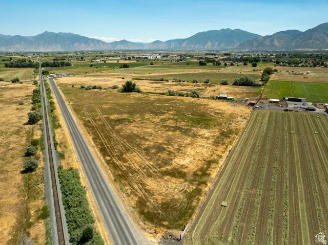 Expansive agricultural land featuring a paved road, railway lines, and distant mountain ranges