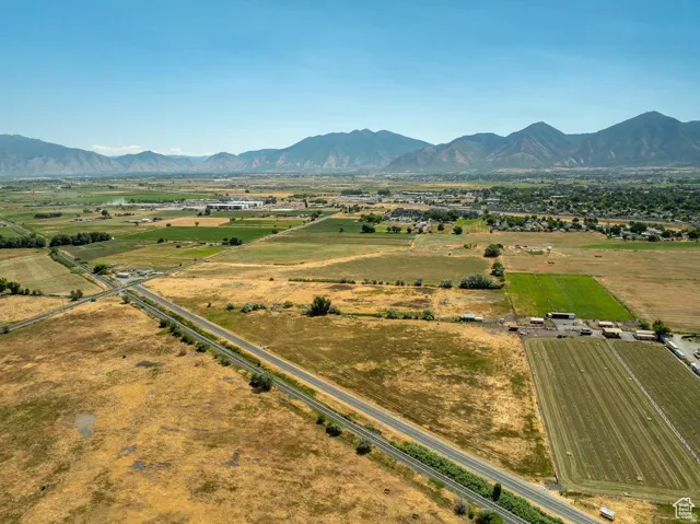 Expansive agricultural land featuring a paved road, cultivated fields, and distant mountain ranges