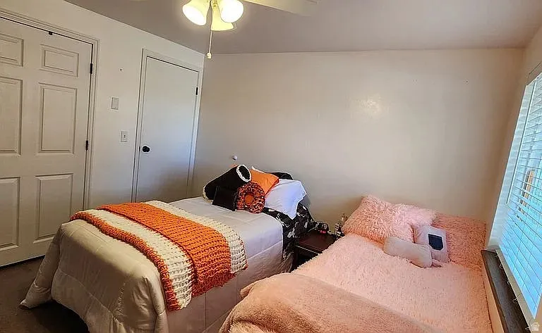 Bright bedroom featuring a ceiling fan with light fixture, two panel doors, and window with blinds