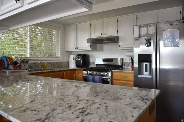 Kitchen featuring extensive light-toned stone countertops, white upper cabinetry, and natural wood-finish lower cabinetry