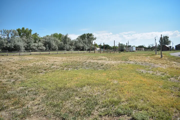 Expansive open lot featuring a wooden split-rail fence and mature trees along the perimeter