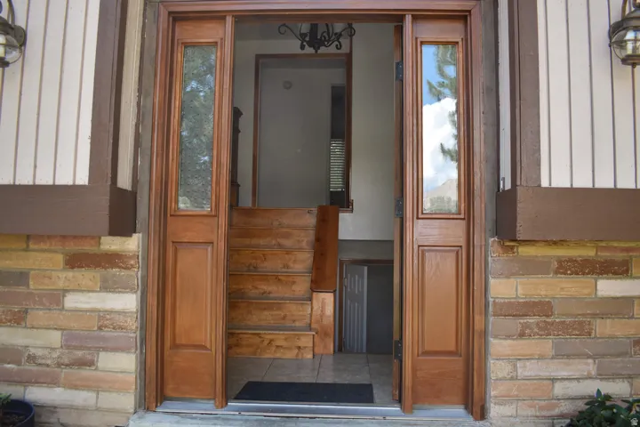 Entryway featuring a wood door with glass side panels, natural wood staircase, brick facade, and vertical siding