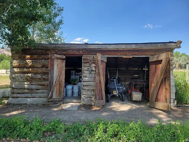 Rustic log outbuilding featuring a durable wood construction, double barn doors, and a gravel floor