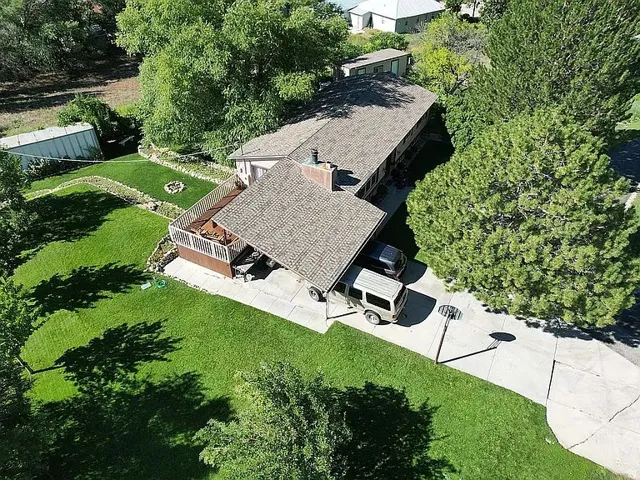 Expansive green lawn surrounds a property featuring a covered patio, multi-level deck, and mature trees