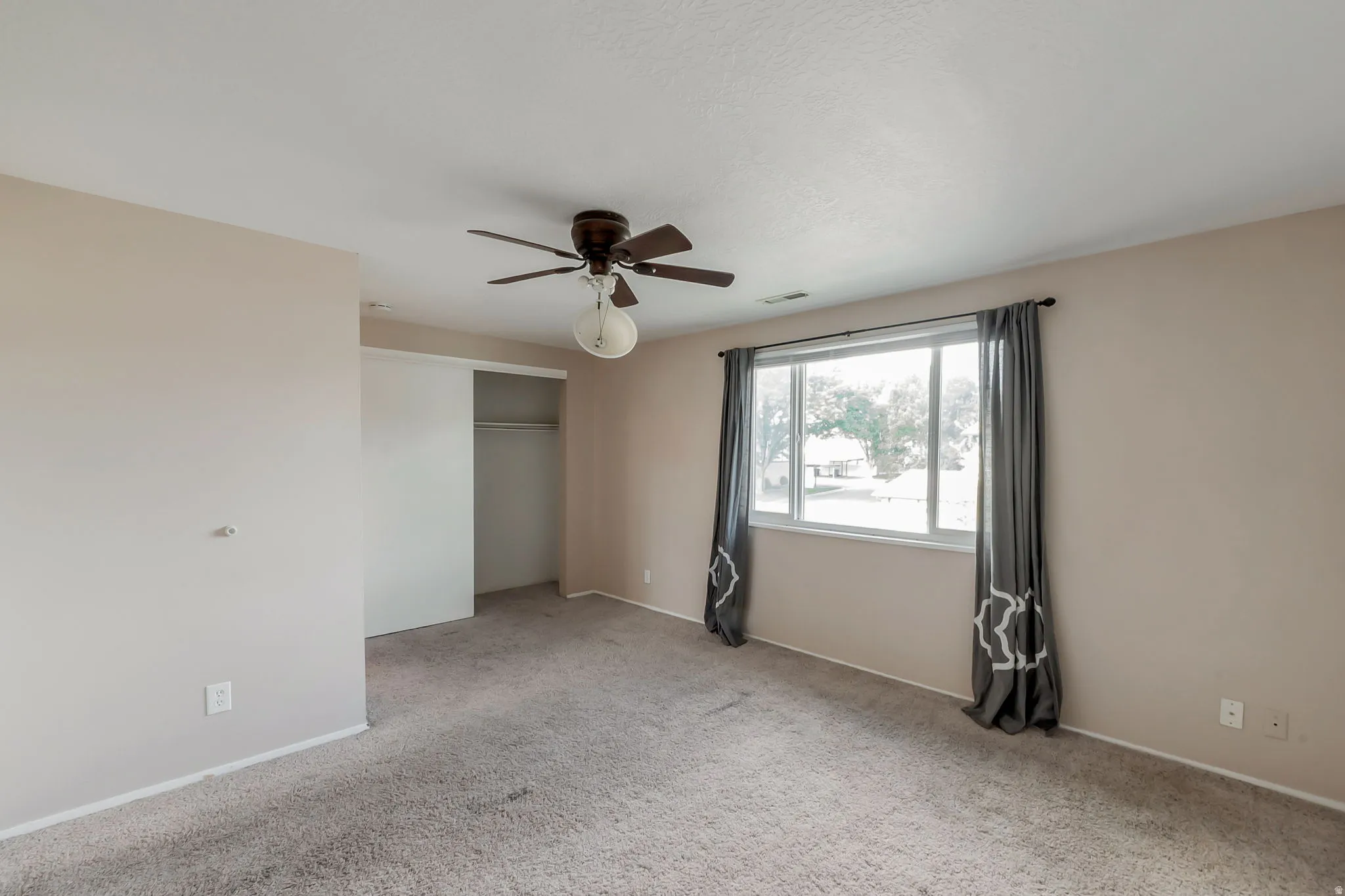 Spacious room featuring neutral carpeting, a large window, and a ceiling fan