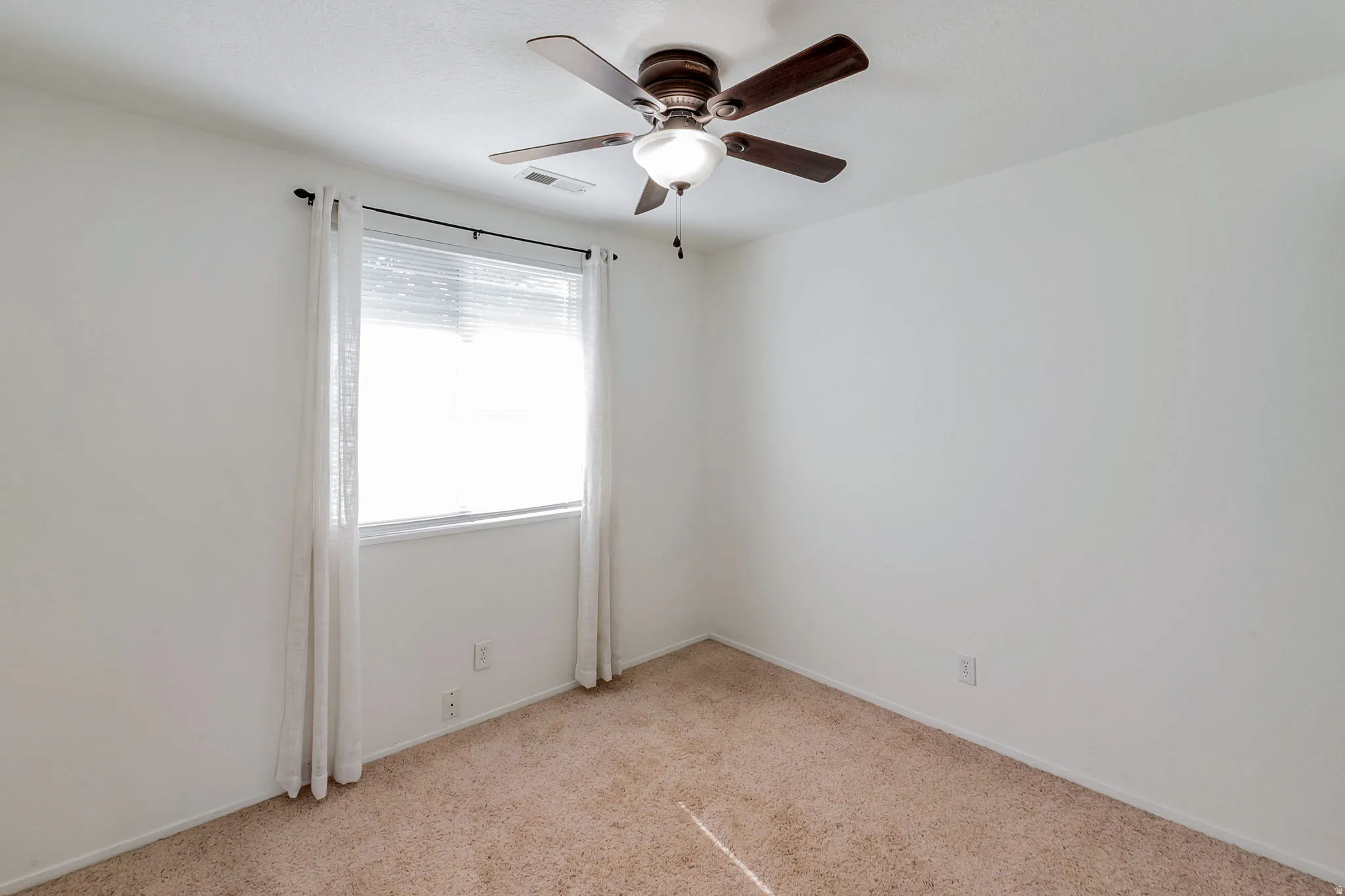 Neutral-toned room featuring a ceiling fan with integrated lighting, a window with blinds, and light-colored carpet flooring