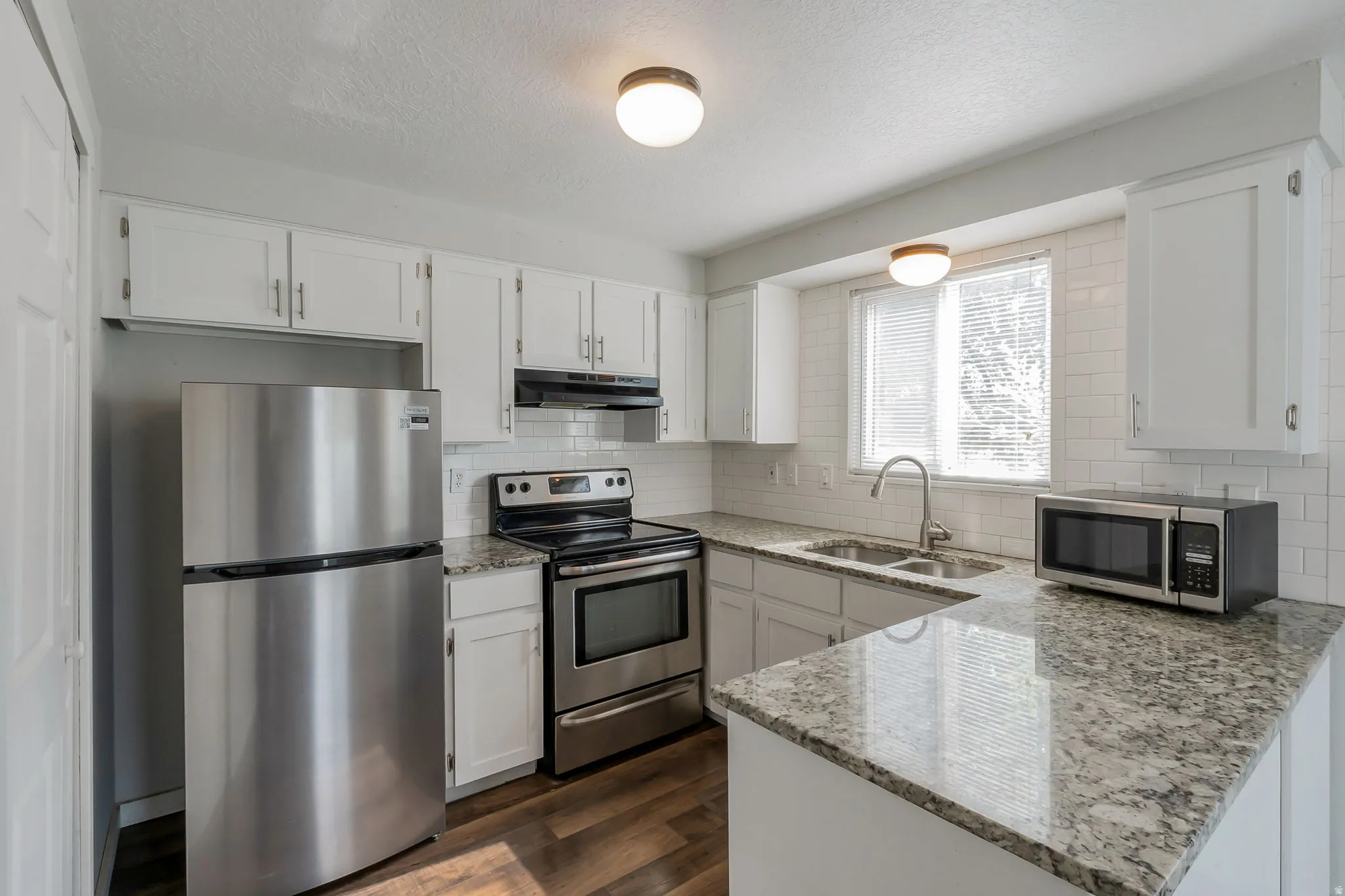 Kitchen featuring stainless steel appliances, white cabinetry, speckled countertops, a double basin sink, and wood-finish flooring
