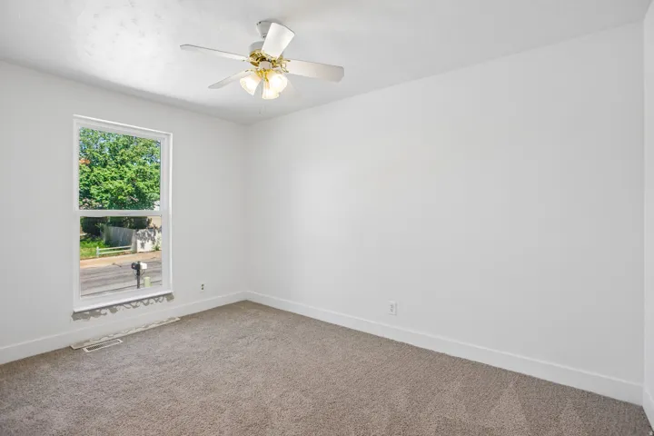 Bright interior space featuring a window, ceiling fan with light fixture, neutral wall finishes, baseboard molding, and carpeted flooring