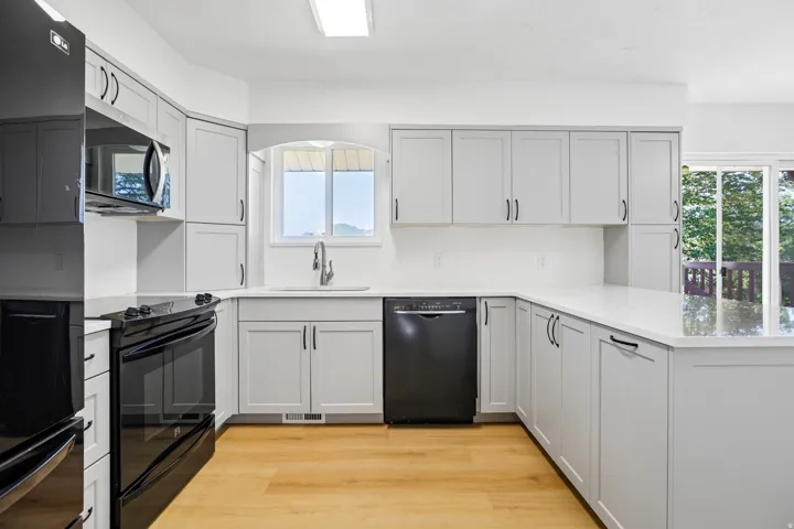 L-shaped kitchen featuring light gray cabinetry, white countertops, black appliances, light wood-finish flooring, and a single-basin sink with a gooseneck faucet