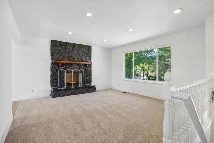 Spacious living area featuring a stone fireplace with a wood mantle, a large multi-pane window, recessed lighting, and neutral carpet flooring