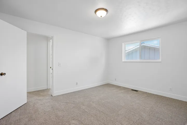 Carpeted room featuring white walls, a single window, and a flush-mount ceiling light fixture