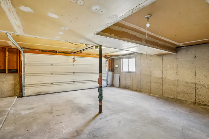 Concrete floor garage with a single garage door, exposed concrete foundation walls, and a small window