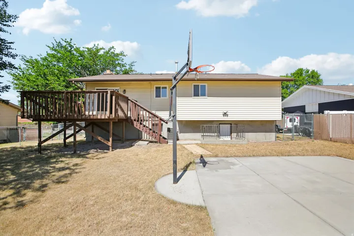 Rear exterior featuring a spacious wood deck with stairs, a concrete patio area, and a basketball hoop