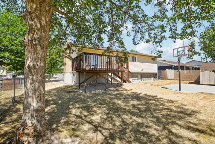 Expansive backyard featuring a wood-decked patio with stairs, a concrete pad, a basketball hoop, and a storage shed