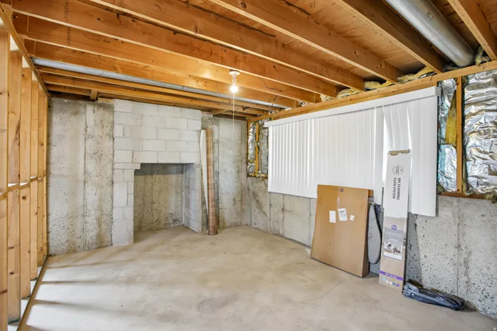 Unfinished basement featuring exposed wood joists, concrete block fireplace structure, poured concrete foundation walls, and a concrete floor