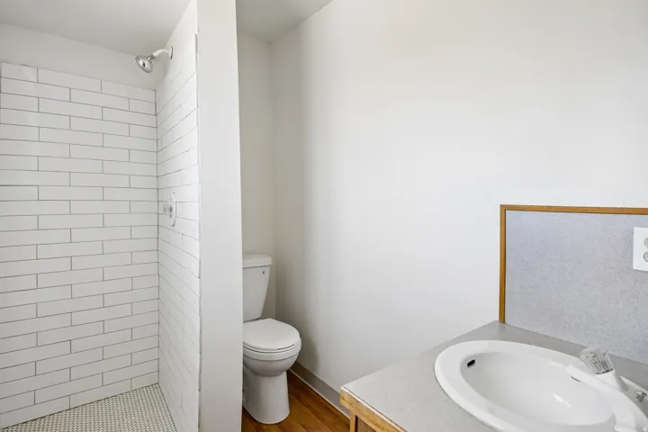Bathroom featuring a white subway tile shower, penny tile shower floor, and a single vanity with an integrated sink and light-colored countertop