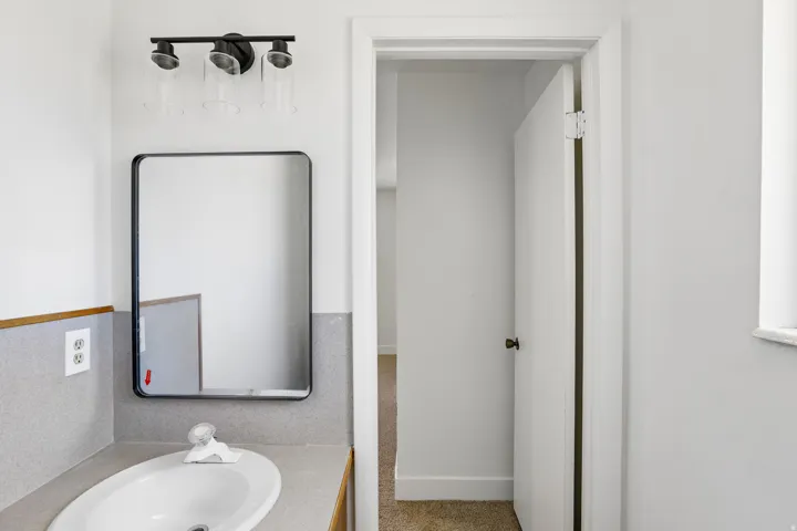 Bathroom vanity featuring a rectangular sink, wall-mounted faucet, and a contemporary black-framed mirror