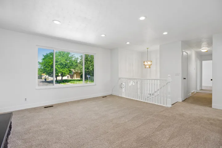 Spacious living area featuring neutral carpeting, a large picture window, recessed lighting, a white baluster railing, and a contemporary chandelier