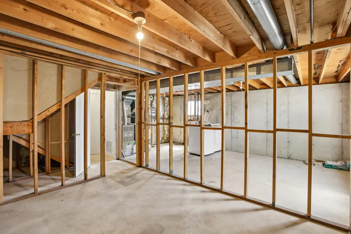 Unfinished basement offering exposed wood framing, concrete flooring, visible overhead joists, and a utility area