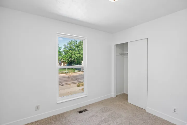 Neutral-toned carpeted room featuring a single window with white trim, a built-in closet with sliding doors, white walls, and white baseboards