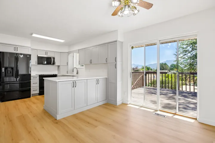 Kitchen featuring light gray cabinetry, white countertops, black appliances, a central island, and wood-finish flooring