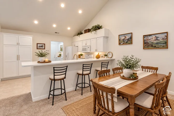 Vaulted ceiling with recessed lighting, white cabinetry, integrated kitchen appliances, white countertop, and a built-in breakfast bar