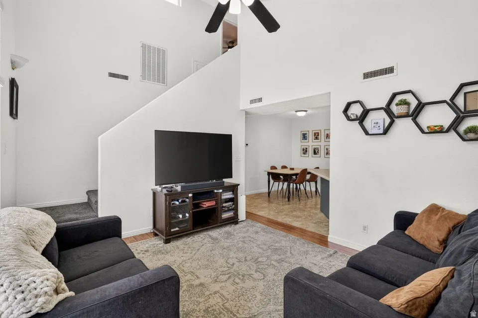 Vaulted ceiling living area featuring a ceiling fan, wood-finish flooring, and a staircase with carpeted treads