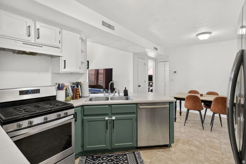 Kitchen featuring stainless steel appliances, dual-tone cabinetry, a double basin sink, and ample counter space
