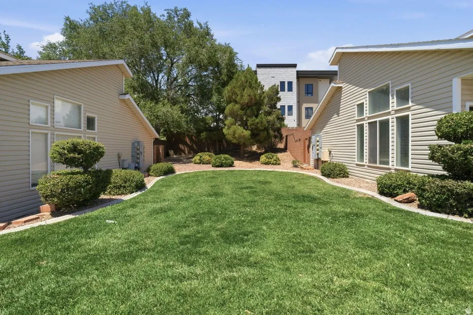 Expansive green lawn framed by landscaping beds with mature shrubs, featuring light-colored siding and multi-pane windows on both structures