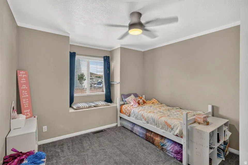 Neutral-toned room featuring a built-in window seat, a ceiling fan with integrated lighting, and textured carpeting