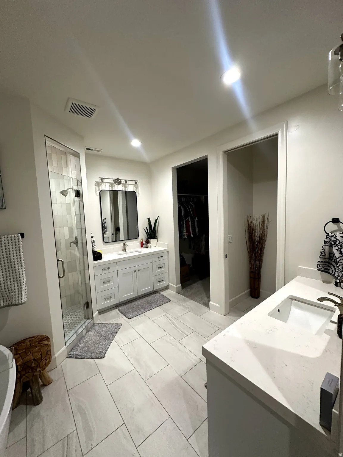 Spacious bathroom featuring light-toned tile flooring, a glass-enclosed shower with tiled walls, and a freestanding soaking tub