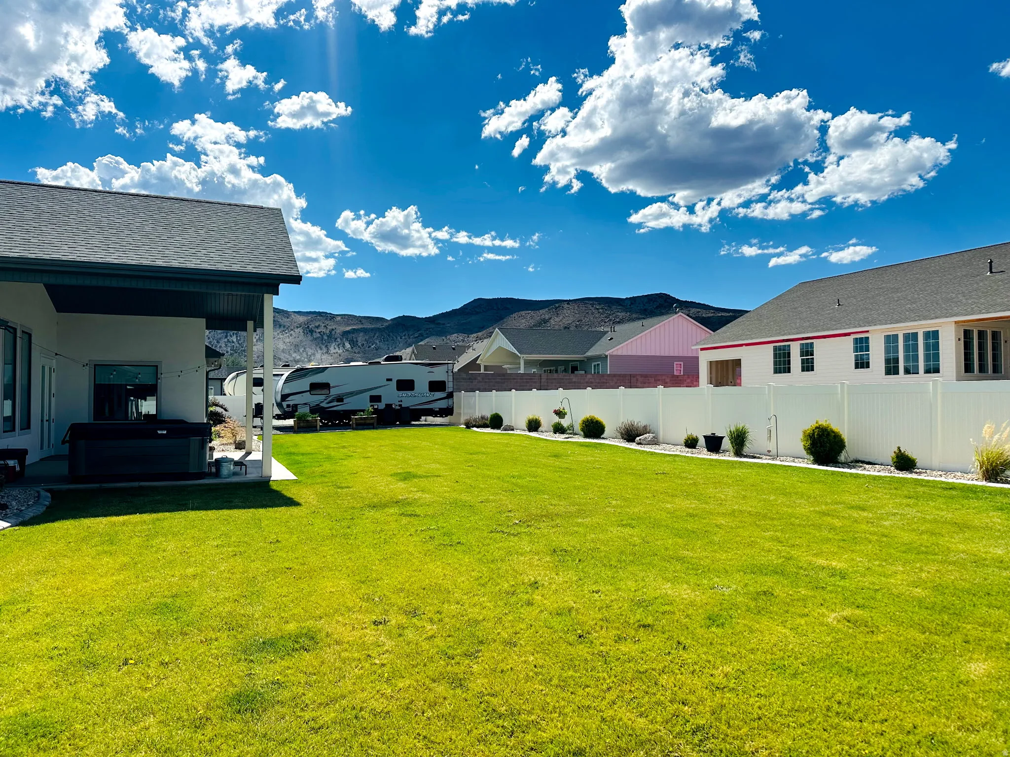 Expansive backyard featuring a manicured lawn, white privacy fencing, and landscaping