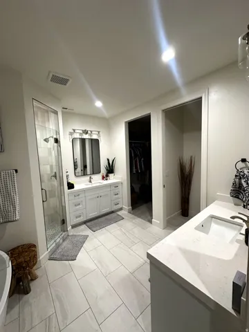 Spacious bathroom featuring light-toned tile flooring, a glass-enclosed shower with tiled walls, and a freestanding soaking tub