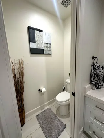 Powder room featuring a white toilet, light-toned walls, and a contemporary wall-mounted abstract art piece