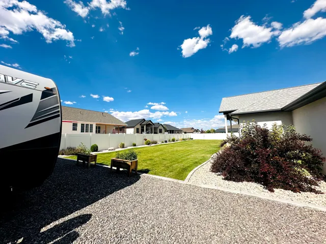 Expansive gravel parking area beside a manicured lawn, bordered by a white privacy fence
