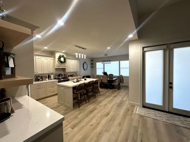 Open-concept kitchen and dining area featuring light-toned cabinetry, quartz countertops, a central island with seating, wood-finish flooring, and recessed lighting